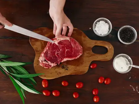 Женщина с ножом в руке нарезает свежее мясо стейка для жарки на кухне