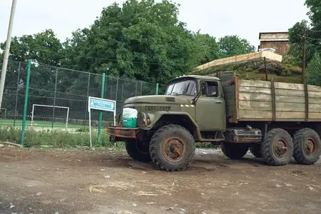 Промышленное транспортное средство с загруженными бревнами стоит на грязном участке на территории лесозаготовительного предприятия, солнечный свет освещает суровый ландшафт и активную транспортную…