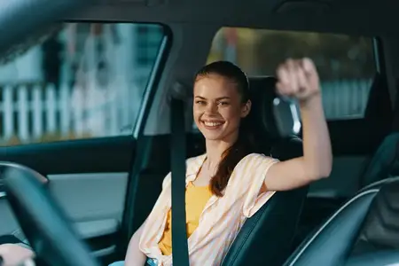 Радостная женщина в автомобиле с весёлым выражением лица, за рулём, излучает ощущение свободы