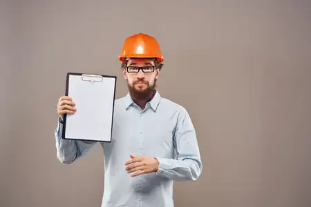 Бородатый мужчина в оранжевой каске, инженер, работает с документами