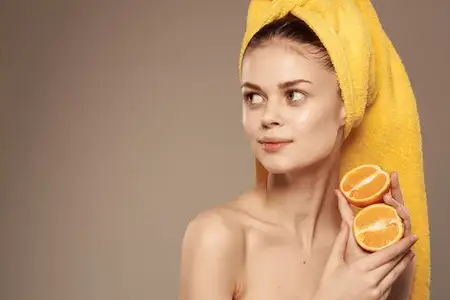Привлекательная женщина с обнаженными плечами держит в руках апельсины, кадрированный вид на бежевом фоне