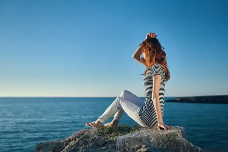 Женщина-туристка на скале у моря на закате, голубое небо и прозрачная вода