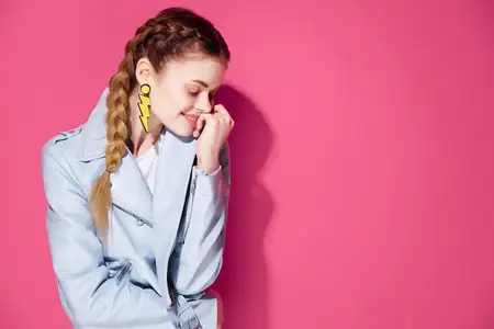 Эмоциональная женщина с косичками, украшения, модная одежда, позирует на розовом фоне