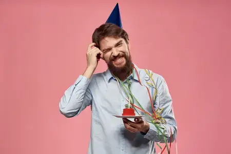 Бородатый мужчина с высунутым языком на розовом фоне, вид крупным планом, на голове синяя кепка