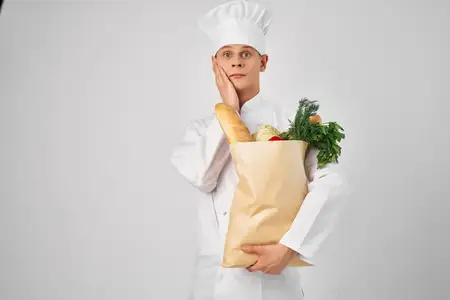 Весёлый мужчина-шеф-повар с пакетом продуктов работает на кухне