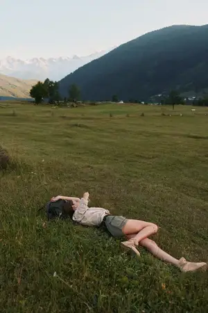 Сцена активного отдыха на природе: женщина отдыхает на траве на фоне холмов, одетая в повседневный летний наряд