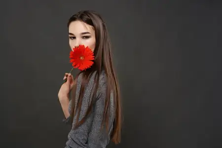 Симпатичная брюнетка с красным цветком у лица, макияж, тёмный фон