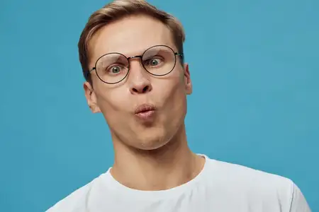 Молодой мужчина европеоидной расы в очках с удивленным выражением лица, одетый в белую футболку, изолирован на синем фоне, концепция гаджетов для психического здоровья, цифровой детокс…