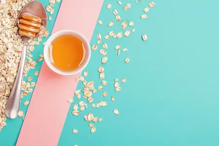 Миска с медом рядом с овсяными хлопьями и ложкой на бирюзово-розовом фоне создает свежий и яркий вид