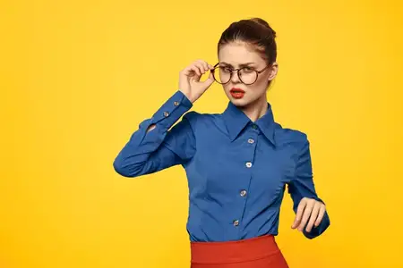Женщина в синей рубашке и красной юбке, в очках, с уверенным выражением лица, портрет на жёлтом фоне, обрезанный вид