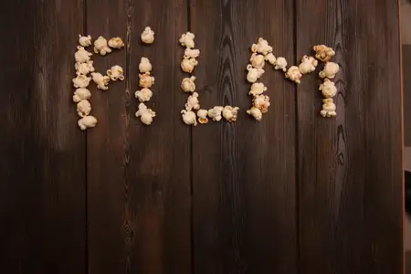 Попкорн выложен в виде слова «movie» (кино) на деревянном фоне