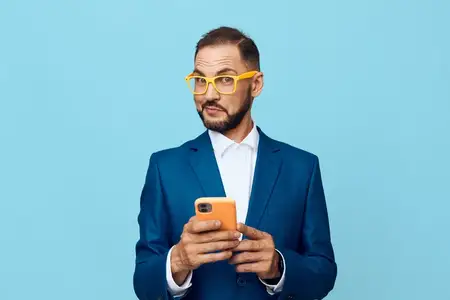 Изолированный цветной фон подчеркивает его выверенную позу, решительный взгляд и тонкие эмоции, когда он взаимодействует с мобильным устройством, изображая деловое мышление, готовность и четкую…