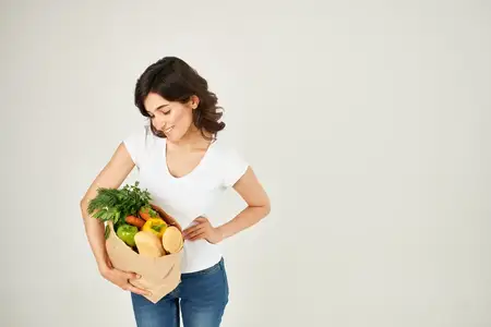 Симпатичная женщина в белой футболке с пакетом продуктов пользуется услугой доставки покупок