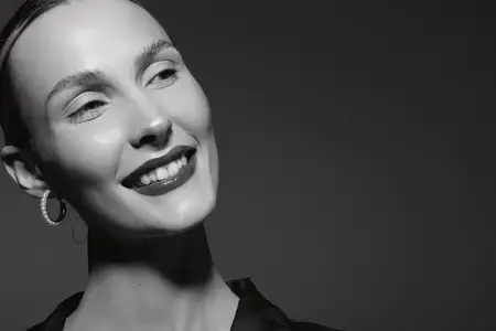 Элегантная белая женщина со светлой кожей мягко улыбается на черно-белом крупном плане, в серьгах-кольцах