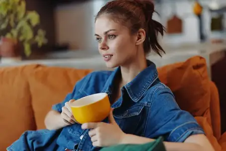 Женщина наслаждается чашкой кофе, отдыхая на диване дома