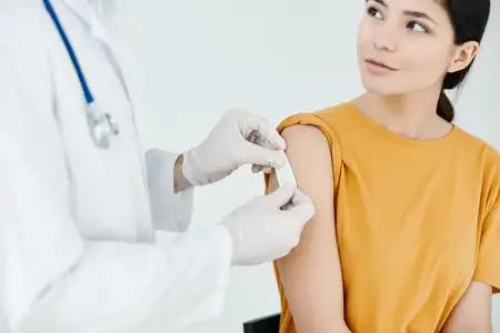 Врач в защитных перчатках наклеивает пластырь после инъекции женщине в желтой футболке
