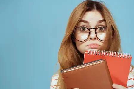 Энергичная студентка с блокнотами и в очках позирует на синем фоне