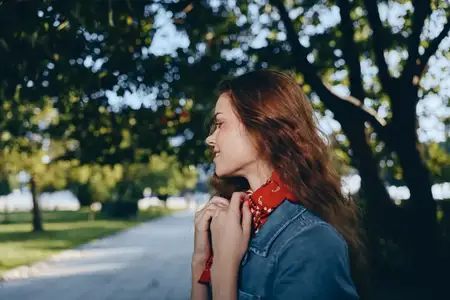 Женщина в стиле casual в современном бохо-вестерн деним стритстайле, позирующая на улице с красным шарфом, в окружении деревьев и естественного света, передающая расслабленное и непринужденное…