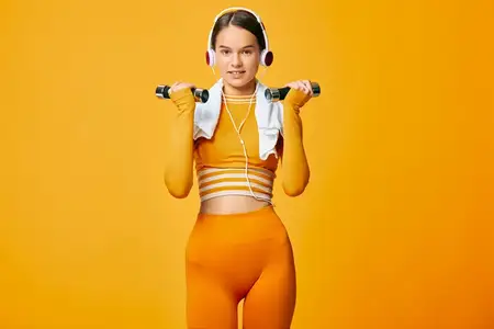 Спортивная женщина в спортивном оранжевом костюме выполняет легкую программу с гантелями, сосредоточенное выражение лица, энергичная тренировочная сцена на ярком цветном фоне