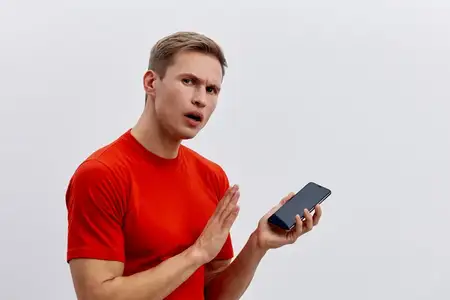 Молодой человек с озадаченным взглядом держит в одной руке смартфон
