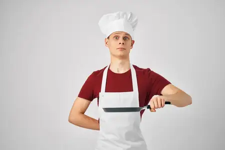 Мужчина-повар в белом фартуке держит сковороду в руках, обрезанный вид профессионала