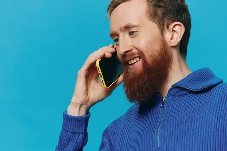 Портрет мужчины с телефоном в руках: он смотрит на экран и разговаривает по телефону на синем фоне