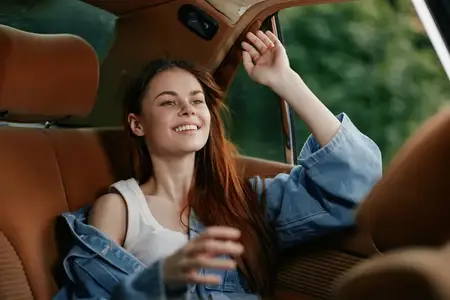 Молодая женщина излучает счастье, сидя в винтажном автомобиле, одетая в стильную джинсовую куртку