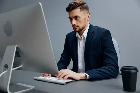 Уставший менеджер с чашкой кофе работает перед компьютером на сером фоне