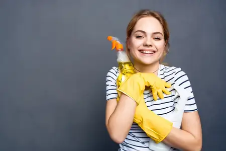 Женщина с моющим средством, тряпками, губками и защитными перчатками