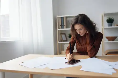 Восхитительная серьёзная задумчивая кудрявая милая леди сидит за столом с бумагами и документами, работая из дома, размышляет о провале бизнеса или банкротстве, рассчитывает бюджет, держит ручку…