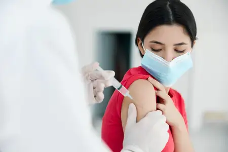 Врач в белом халате делает инъекцию в плечо пациенту в медицинской маске