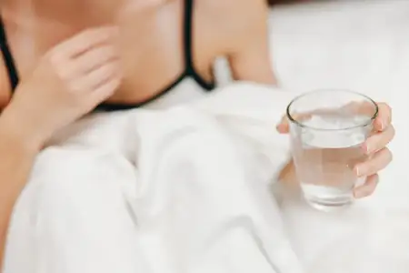 Женщина отдыхает в постели со стаканом воды на белых простынях и одеяле