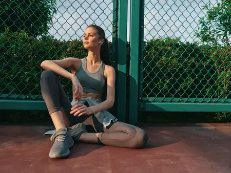 Подтянутая женщина в спортивной одежде отдыхает на корте, наслаждаясь солнечным светом