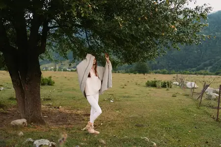 Непринужденный жизненный кадр женщины, наслаждающейся природой, сельский пейзаж с травой и деревьями, повседневная мода, спокойное настроение, яркий дневной свет, безмятежная и беззаботная атмосфера