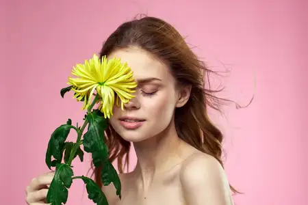 Красивая девушка с жёлтым цветком на розовом фоне, обнажённые плечи, макияж