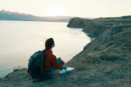 Женщина-туристка сидит на земле в горах у моря на закате