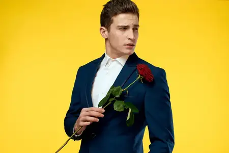 Джентльмен в классическом костюме на жёлтом фоне с красной розой, романтика, обрезанный вид, модель, портрет