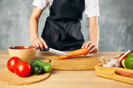 Женщина в черном фартуке на кухне нарезает овощи