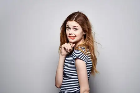 Жизнерадостная женщина держится за волосы, наносит макияж, позирует с веселым настроением в модном образе на изолированном фоне