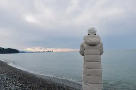 Одиночество, береговая линия, зима, созерцание, морской пейзаж, человек в длинном пальто смотрит на горизонт, пока накатывают волны под серым небом