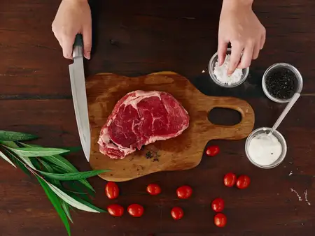 Женщина с ножом в руке нарезает свежий стейк для жарки на кухне