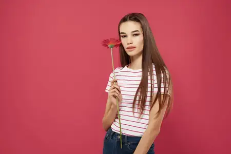 Симпатичная брюнетка в розовой шляпе с цветком позирует на изолированном фоне