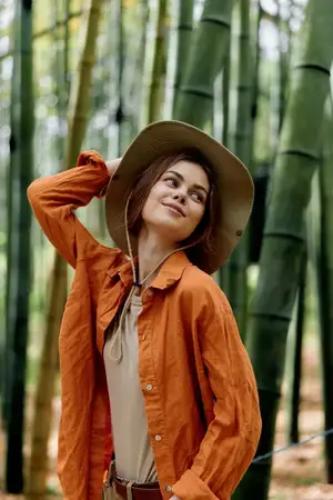 Женщина в шляпе в бамбуковом лесу, портрет на природе, в куртке, с улыбкой, путешествующая на фоне зеленой листвы, безмятежных солнечных лучей и стеблей
