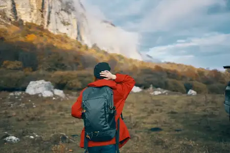 Женщина на фоне горного пейзажа, в отпуске, с рюкзаком, занимается туризмом, на ней шляпа, в небе облака