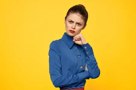 Портрет женщины в голубой рубашке с ярким макияжем, красными губами, на жёлтом фоне, обрезанный вид