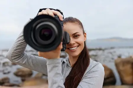 Веселая молодая женщина занимается фотографией на пляже, держа камеру близко к лицу