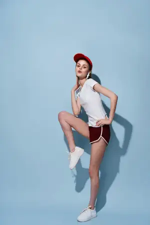 Весёлая девушка в белой футболке и шортах позирует для модной фотографии в полный рост