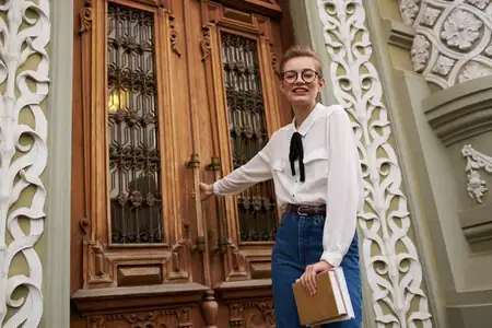 Студент в очках прогуливается по городу с книгой в руках, общаясь с окружающим миром
