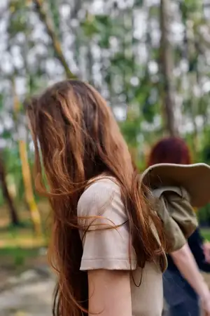 Женщина с длинными волосами в лесу на природе, с рюкзаком на плече во время прогулки с попутчиком, откровенный боковой портрет молодой девушки-подростка в парковой обстановке с мягким боке листьев
