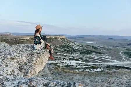 Безмятежная женщина любуется захватывающим дух закатом над долиной и горами, сидя на скалистом уступе